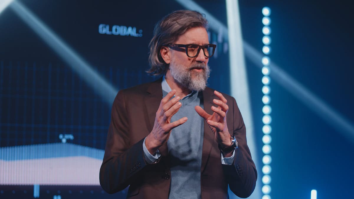 A bearded man leads a presentation in front of a large screen.