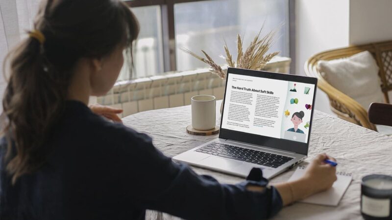 A woman reads a whitepaper on her laptop while taking notes on a piece of paper.