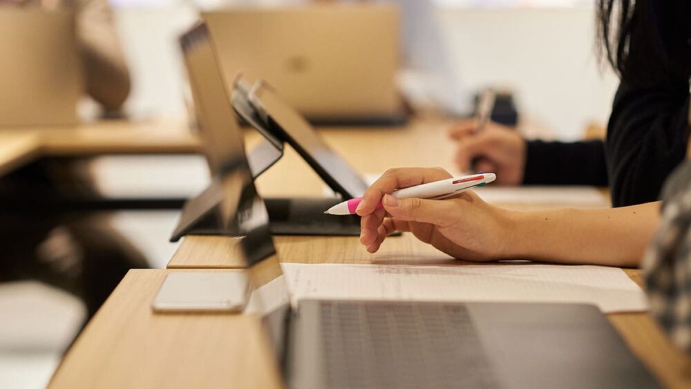 A closeup of someone holding a pen to take notes next to their open laptop.