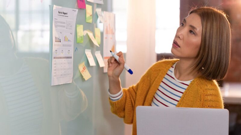 An Asian woman reviews sticky notes and prepares for a presentation.