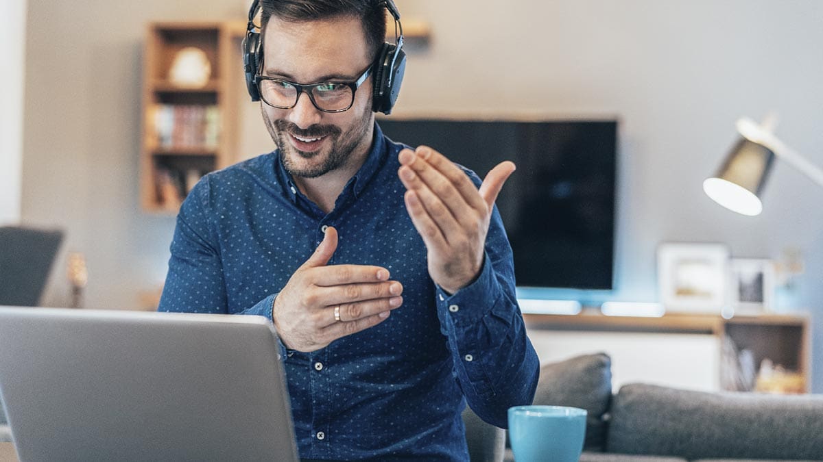 A man in a virtual meeting with headphones and a laptop is talking.