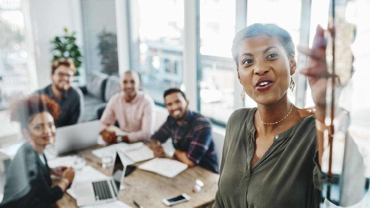 A Black woman leads a presentation in front of a small group of people in a conference room.