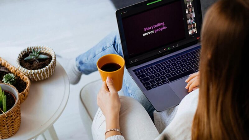 A woman holding a cup of coffee is watching a virtual presentation on her laptop.