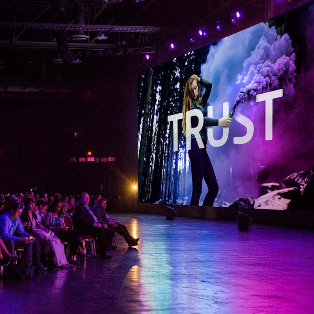The stage for a large Keynote event, with a large audience and a large image on a screen that reads "Trust".