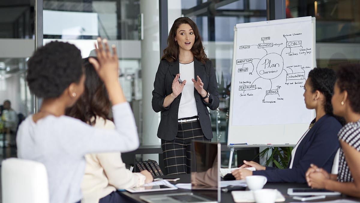 A woman leads a presentation in front of a conference room of people.