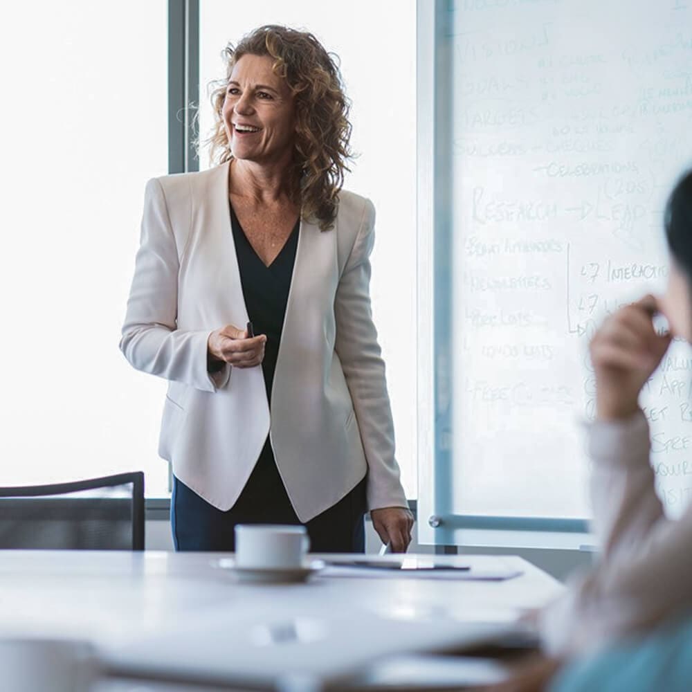 A smiling woman standing up in a conference room, leading a Sales Enablement consultation.